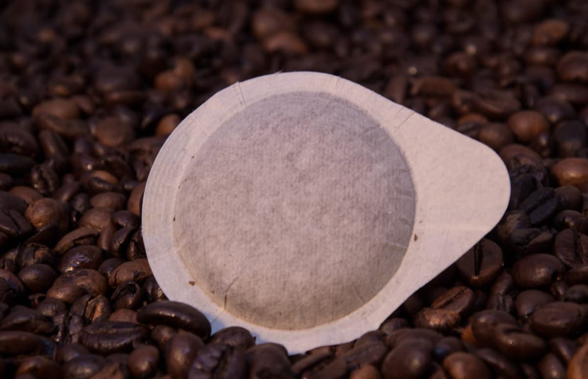 Cialda ESE in filtro di carta su un letto di chicchi di caffè