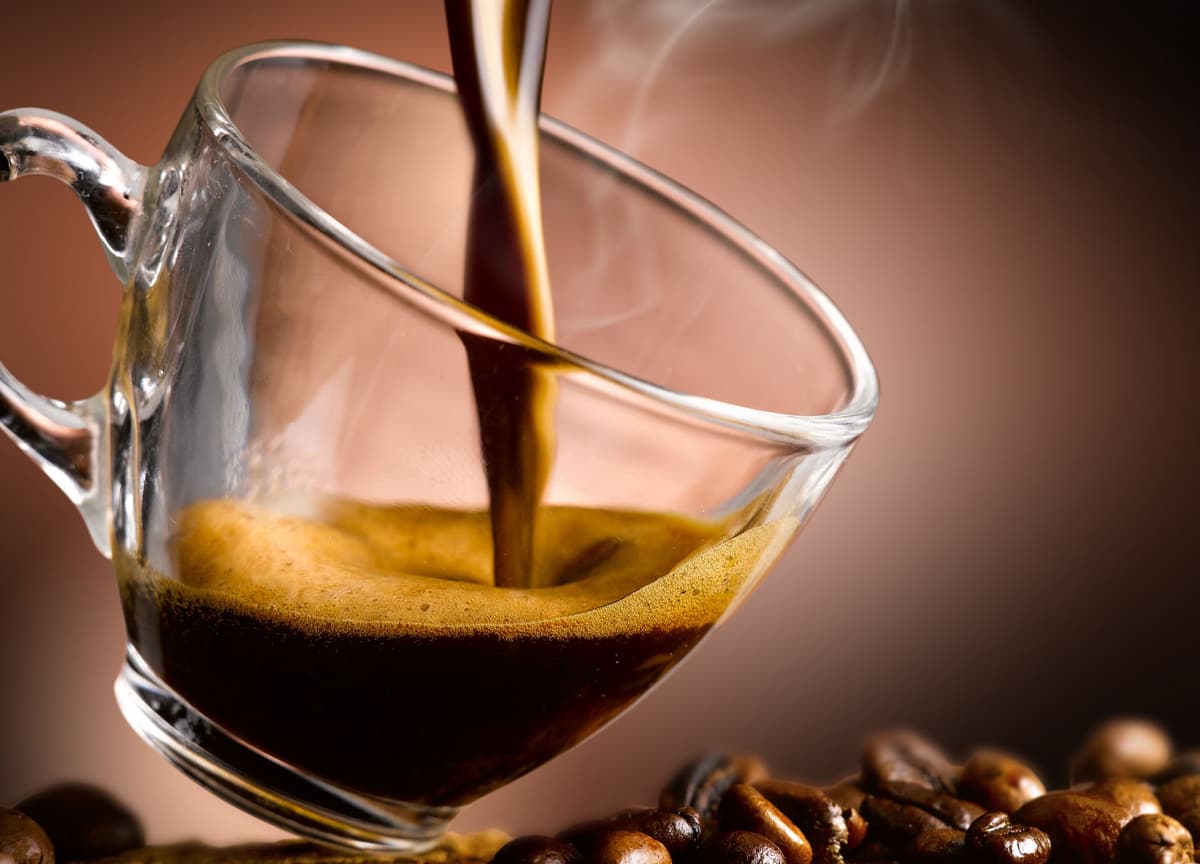 Caffè che scende fumante dentro una tazza di vetro